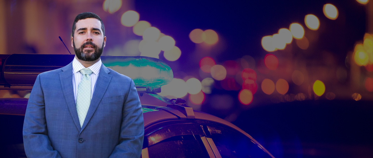 Profile photo of Rudy 'Glynn' Vrba, with a background photograph focused on the sirens of a police car against a blurry backdrop of street lights.